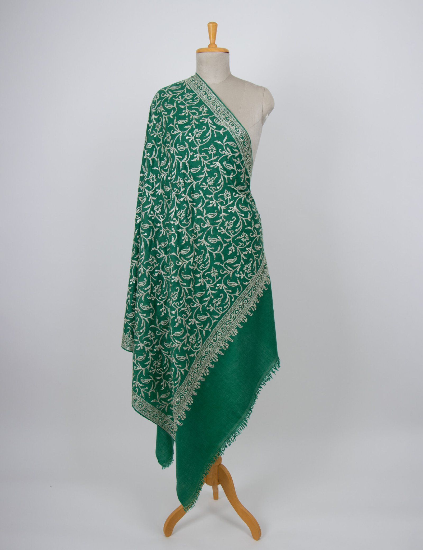 A draped emerald green pure pashmina shawl featuring a shimmering hand-embroidered silver Tilla metallic thread border and soft cashmere texture.